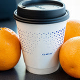 12 oz Custom Printed Recyclable Double Walled Paper Cups with Calarity Logo next to oranges. Printed by The Cup Store