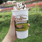 16 oz. Multicolor Recyclable Paper Cup displaying "Coffee House", posed with a hand, outdoors.
