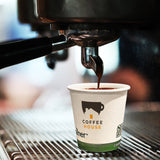 4 oz paper cup with green bottom stripe and "Coffee House" logo with cup and house graphic, in coffee machine being filled with coffee