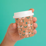 8 oz. Full Wrap Recyclable Paper Cup displaying "caffe", held in front of a teal background.