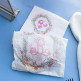 Two white paper sandwich bags with a floral border and the letter 'R' printed, one lying flat on a blue table and the other closed with contents inside