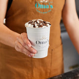 Paper coffee cup with a white coffee Sleeve that has a "Oma's cafe & wine bar" logo, being served by a barista