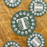 Round green coaster with a "T" logo, decorated with icons of wines and hops, four green coasters in the background on the table
