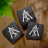 Three black square coasters with "As the structure fails" logo printed in white, on a wooden table