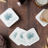 Five square coasters with blue "The Islands of Islamorada" logo and illustration of a leaf fan, on a wooden table next to two glasses
