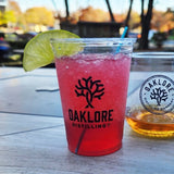 10 oz Oaklore plastic cup with red sparkling drink and lime, wooden table outdoors with orange drink behind