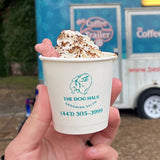 Custom printed 4 oz paper cup with blue "The Dog Haus Grooming Salon" logo and dog print, filled with whipped cream and bone snack, held by hand