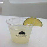 9 oz plastic cup filled with lemonade-like drink, garnished with lime, on white table