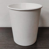 Blank white 10 oz paper cup on grey wooden table, white wall in background