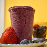 10 oz blank plastic cup filled with red smoothie, on plate with strawberries and blueberries on yellow background