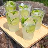 Top view of five 10 oz recyclable plastic cups with clear drinks, lime, ice, and mint on wooden tray