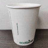 12 oz compostable paper cup with green "ecotainer" and "Caution: Contents Hot" text, on grey wooden table with clean white wall background