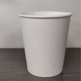 Blank white 12 oz paper cup on grey wooden table, white wall in background