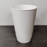 Blank white 16 oz premium double walled paper cup on grey wooden table, white wall in background