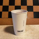 16 oz double-walled paper cup filled with tea, standing on marble table, brown and black checkered wall in background