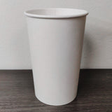 Blank white 16 oz paper cup on grey wooden table, white wall in background