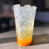 32 oz plastic cup, filled with shimmering lemonade with orange syrup and ice, on wooden table