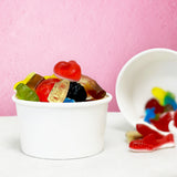 Two 5 oz paper food containers, filled with gummy candy, with one on its side, standing on white table with pink background