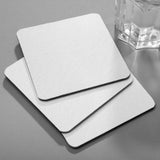 Three 4" Blank Medium Weight Square Coaster, in a fanned out stack, beside a glass of water, on a grey background