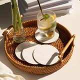 Four blank medium weight round coasters in a woven basket, with a glass  cup filled with water and a vase, on a white table
