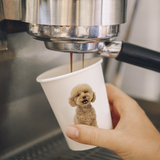 12 oz. Multicolor Recyclable Paper Cup displaying a poodle, being held and filled under a espresso machine.