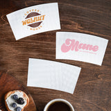 Three White Coffee Sleeve of varying logos beside a cup of coffee and wooden tray of desserts, on a wooden table