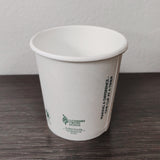 4 oz compostable paper cup showing seam, with green text printed, on grey wooden table, white wall background