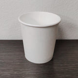 Blank white 4 oz paper cup on grey wooden table, white wall in background