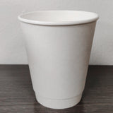 Blank white 8 oz premium double walled paper cup on grey wooden table, white wall in background