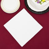 Blank 3-PLY White Dinner Napkin next to a stack of white paper plates and black tray with an entire cake, on a red table cloth