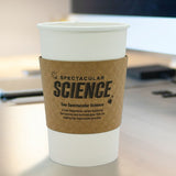 White, paper cup with Kraft Brown Coffee Sleeve displaying "Spectacular Science" logo, on a brown office desk